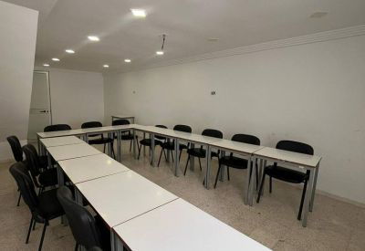 Conference room setup with white tables arranged in a U-shape and black office chairs.
