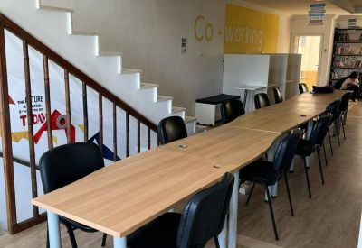 Coworking space with long wooden tables and black chairs next to a white staircase.