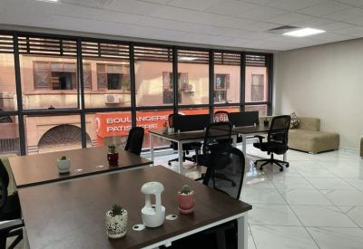 Open office area featuring multiple wooden desks, ergonomic chairs, and city view windows.