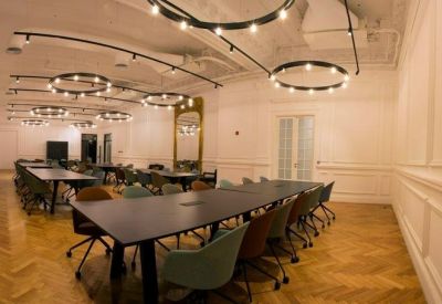 Large communal coworking space with long black tables and distinctive halo light fixtures.