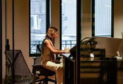 Private glass-walled office pod with a person working at a dark desk.