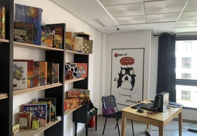 Office workstation with a computer desk and shelves stocked with various board games.