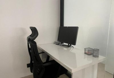 Single workstation with an ergonomic black mesh chair and a white desk against a minimalist wall.