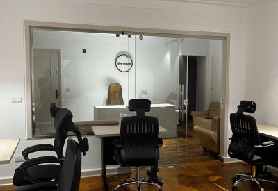 View through a glass partition showing an office interior with wooden floors and tan armchairs.