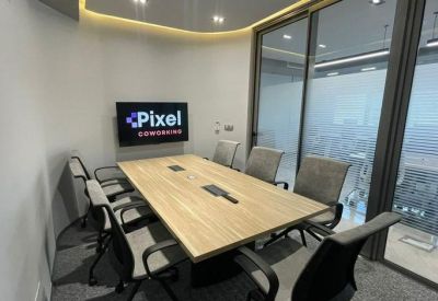 Meeting room with a light wood table, grey chairs, and a TV displaying the Pixel Coworking logo.