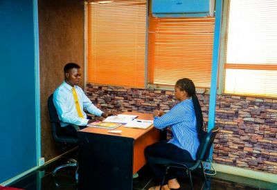 Private consultation room with a wooden desk and two chairs against a brick-patterned wall.