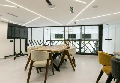Meeting room with a long wooden table, comfortable chairs, and modern strip lighting on the ceiling.