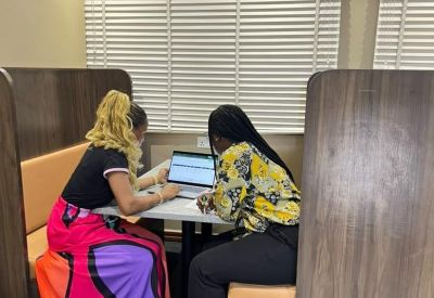 Two people working on a laptop in a private wood-paneled booth with colorful seating.