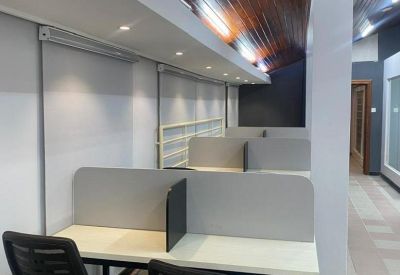 Modern open-plan workspace with white desks, black chairs, and a polished wood ceiling.