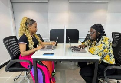 Two professionals collaborating at a shared desk with privacy dividers and rolling chairs.