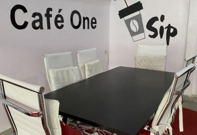 Private meeting room with a black table, white leather chairs, and branded Cafe One wall art.