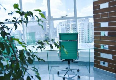 Private office workstation with a green chair and glass desk overlooking city buildings.