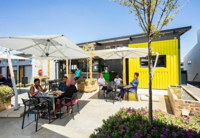 Sunny outdoor courtyard with seating area, large umbrellas, and bright yellow feature wall.