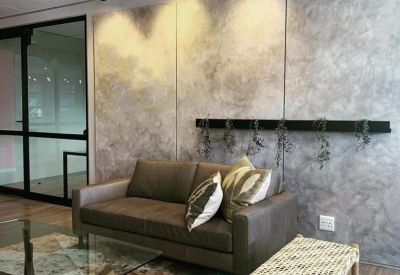 Lounge area with a dark leather sofa, patterned cushions, and a textured concrete-style feature wall.