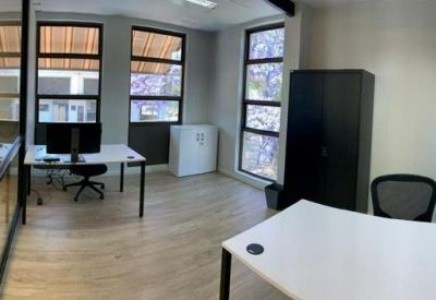 Private office suite with white desks, black chairs, and large windows overlooking trees.