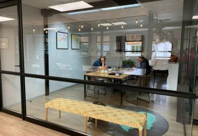 Glass-walled meeting room with a wooden table, woven bench, and decorative string lighting.