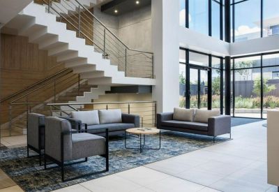 Lounge area with grey sofas and a wooden staircase in a bright, multi-story atrium.