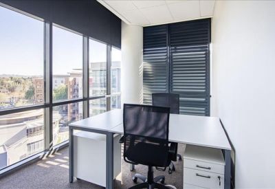 Private office suite featuring a white desk, ergonomic chair, and large windows with city views.