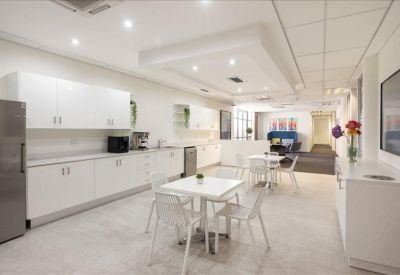 Modern communal kitchen and dining area featuring white cabinetry and bistro seating.