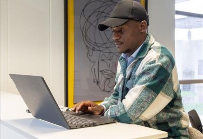 A man working on a laptop at a white desk in front of framed line art.