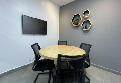 Meeting room featuring a round wooden table, black mesh chairs, and hexagonal wall shelving.