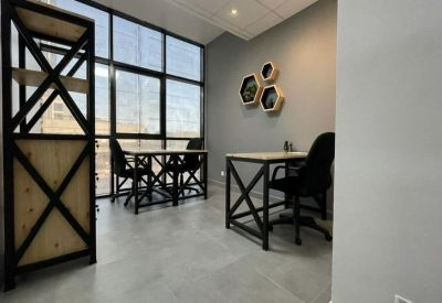 Office interior showing modern wooden workstations and a tall industrial-style shelving unit by large windows.