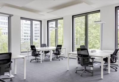 Spacious open-plan office with white desks, ergonomic chairs, and large windows overlooking city buildings.