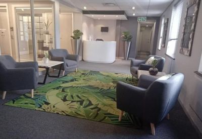 Welcoming reception area with a leaf-patterned green rug and grey armchairs.
