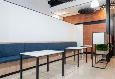 Breakout area with long blue cushioned bench seating, white tables, and brick wall accents.