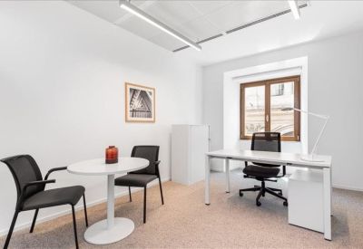 Bright private office featuring a white desk, ergonomic chair, and a small round discussion table.