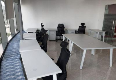 Open-plan office area with several white workstations and black ergonomic chairs.