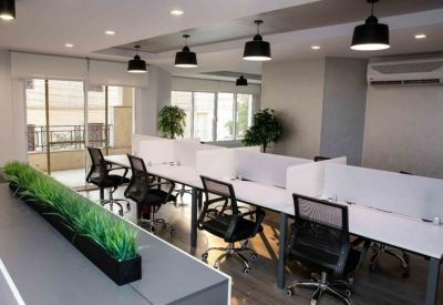 Open-plan workspace with long white desks, black chairs, and decorative greenery.