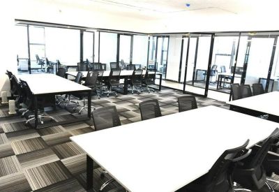 Bright, open-plan office space featuring white desks and glass-walled private suites.