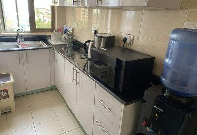 Compact modern kitchen with white cabinetry, black countertops, and a water dispenser.