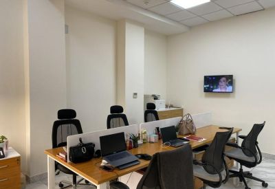 Open-plan office with wooden desks, ergonomic black chairs, and a wall-mounted television.