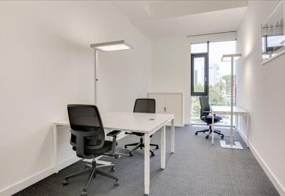 Minimalist private office with two white desks and black mesh chairs.