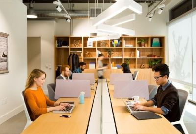 Shared office space with long wooden desks and integrated privacy screens.