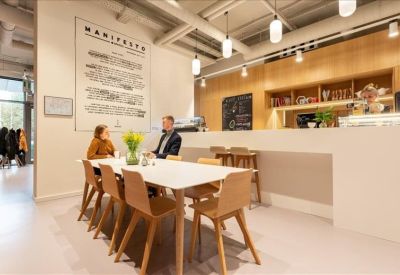 Bright café area with a long white communal table and modern wooden chairs.