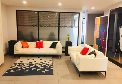 Bright communal lounge with white sofas, colorful pillows, and a geometric patterned rug.