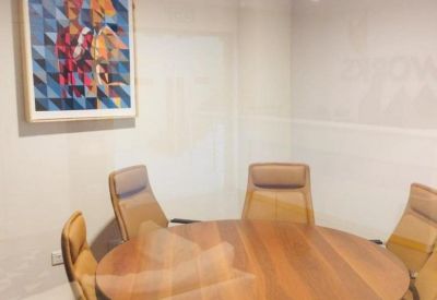 Private meeting room featuring a round wooden table and tan leather chairs behind glass walls.