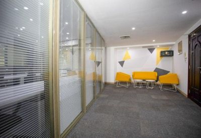Hallway view showing glass-partitioned offices and a yellow seating area.