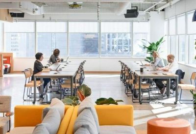 Open-plan coworking space with long communal desks and large windows.