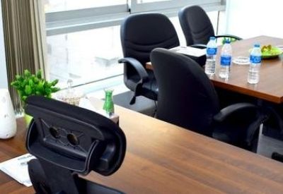 Meeting room with wooden tables, black ergonomic chairs, and bottled water.