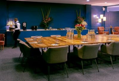 Spacious boardroom featuring a large wooden table, plush grey chairs, and a deep blue feature wall.