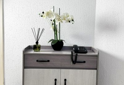 Light wood storage cabinet topped with orchids and a framed floral print.