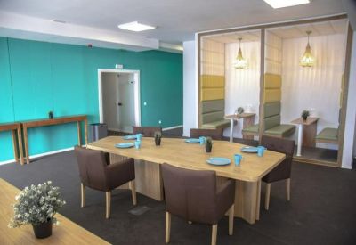 Communal breakout space with a teal feature wall, large wooden table, and private seating booths.
