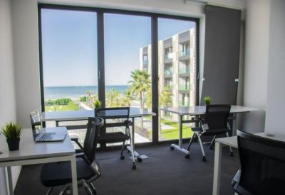 Bright office with multiple workstations featuring large windows overlooking the ocean.