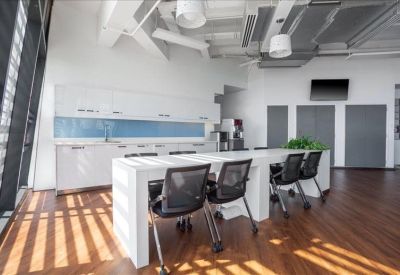 Modern communal kitchen and dining area with wood-style flooring and sleek white cabinetry.