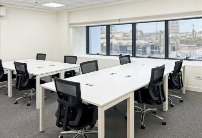 Bright open-plan office with white desks, black ergonomic chairs, and large windows with city views.