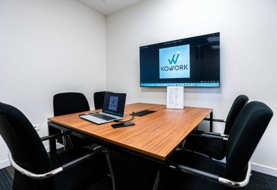 Small meeting room with a wooden table, wall-mounted screen, and four black chairs.